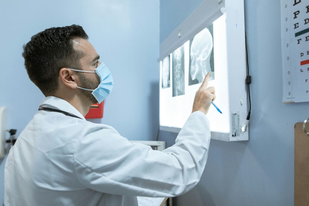 A healthcare professional examines brain X-rays while wearing a face mask in a hospital setting.